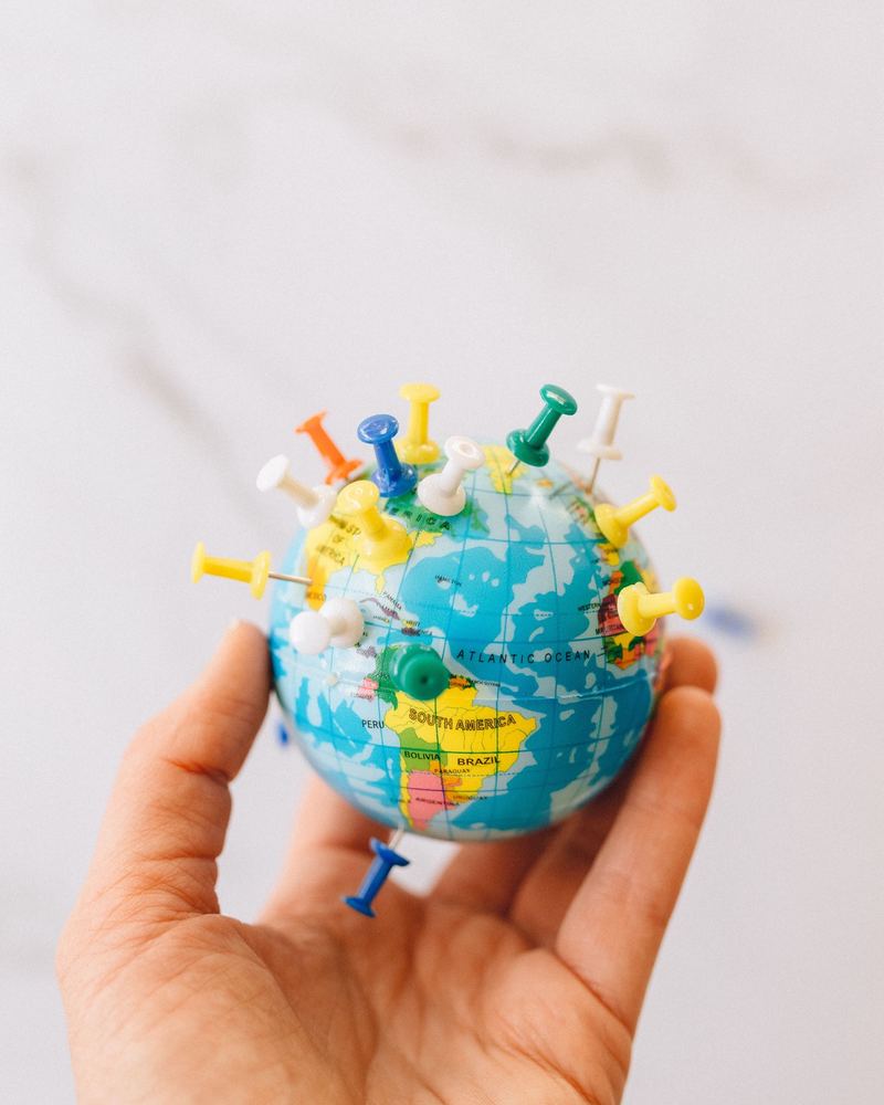 A hand holding a small globe marked with pins across three continents